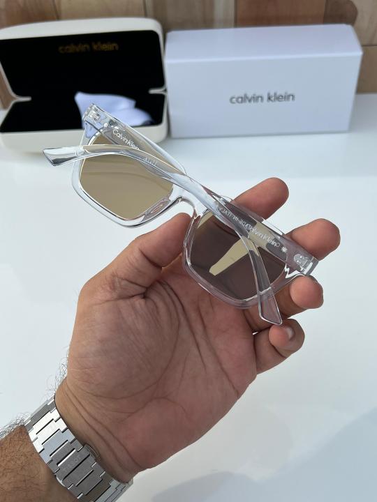 Calvin Klein square sunglasses with a clear/transparent frame and brown lenses.