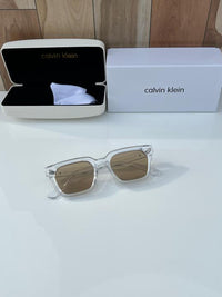 Calvin Klein square sunglasses with a clear/transparent frame and brown lenses.